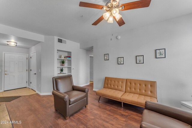 living room featuring built in shelves, wood-type flooring, and ceiling fan