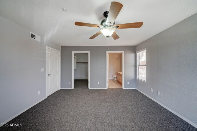 unfurnished bedroom with a spacious closet, light colored carpet, ceiling fan, ensuite bath, and a closet