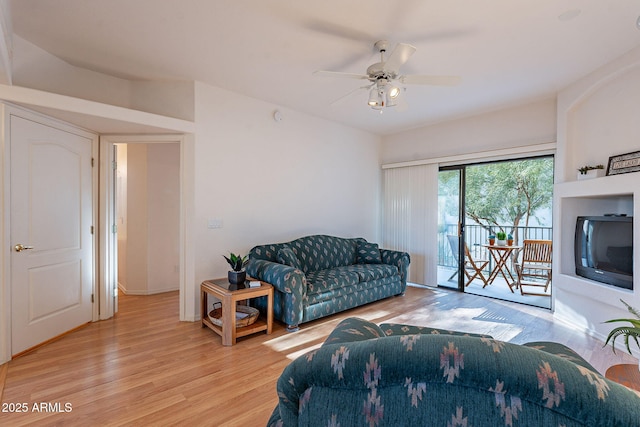 living area featuring light wood-type flooring, a glass covered fireplace, and ceiling fan