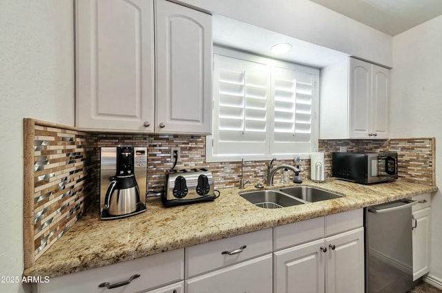 kitchen featuring light stone counters, stainless steel appliances, a sink, white cabinetry, and backsplash