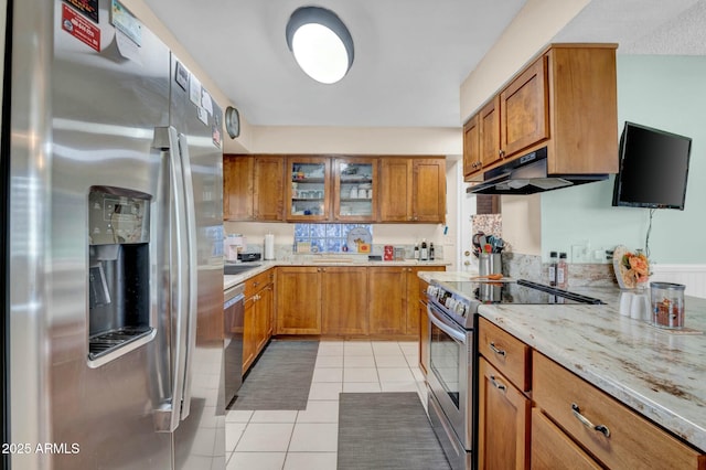 kitchen with under cabinet range hood, light tile patterned floors, appliances with stainless steel finishes, and brown cabinets