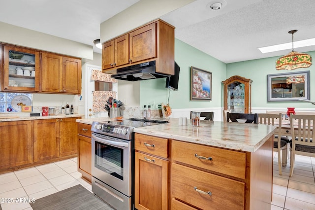 kitchen with light tile patterned floors, electric stove, brown cabinetry, and under cabinet range hood