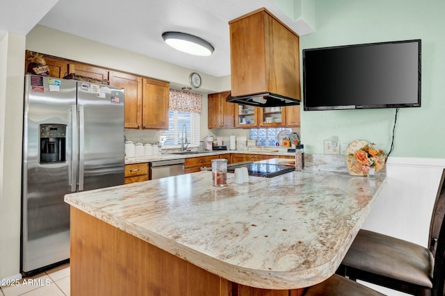 kitchen featuring stainless steel appliances, brown cabinetry, a sink, a peninsula, and a kitchen bar