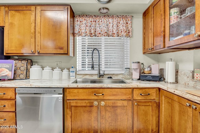 kitchen with brown cabinetry, dishwasher, a sink, and light stone countertops