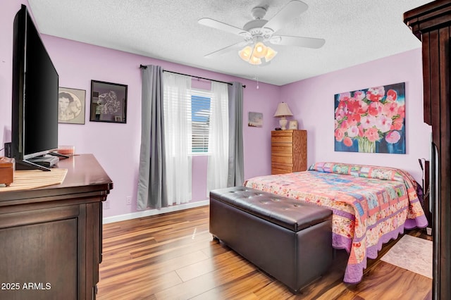 bedroom with a ceiling fan, a textured ceiling, baseboards, and wood finished floors