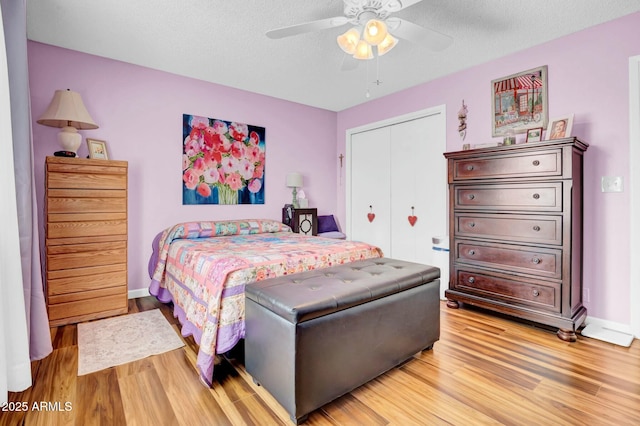 bedroom featuring light wood-type flooring, a textured ceiling, baseboards, and a closet