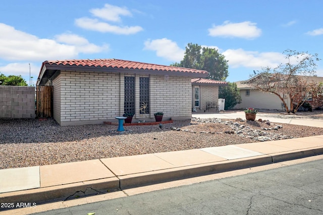 view of front of home featuring a patio area, brick siding, fence, and a tiled roof