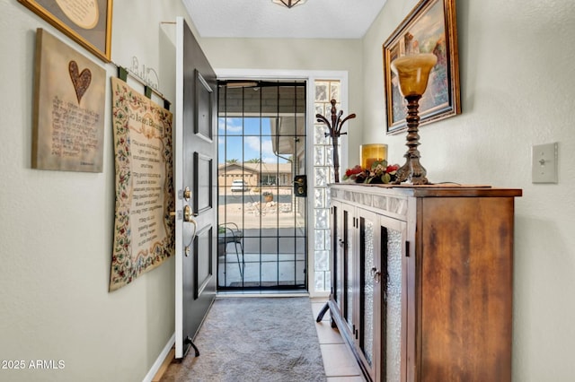 doorway to outside featuring carpet, baseboards, and a textured ceiling