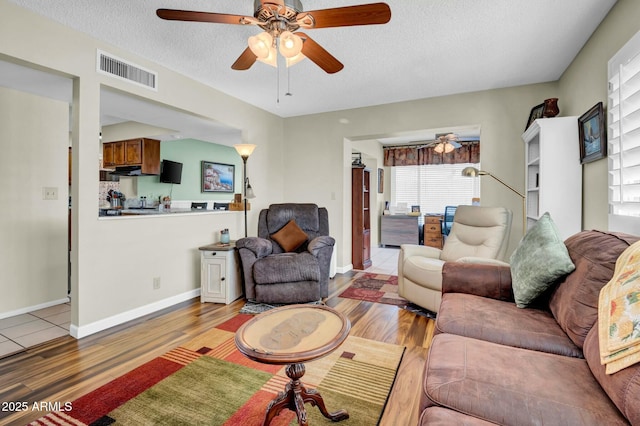 living room featuring visible vents, ceiling fan, a textured ceiling, light wood-type flooring, and baseboards