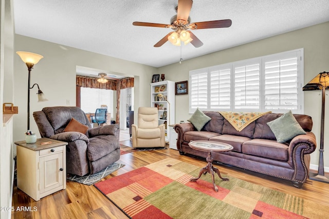 living room with light wood-type flooring, ceiling fan, and a textured ceiling