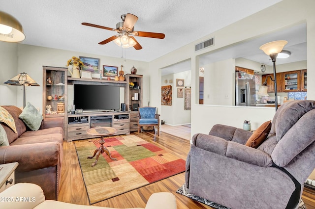 living area with a ceiling fan, a textured ceiling, visible vents, and wood finished floors