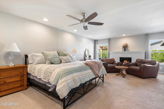 bedroom with recessed lighting, light colored carpet, a warm lit fireplace, and ceiling fan