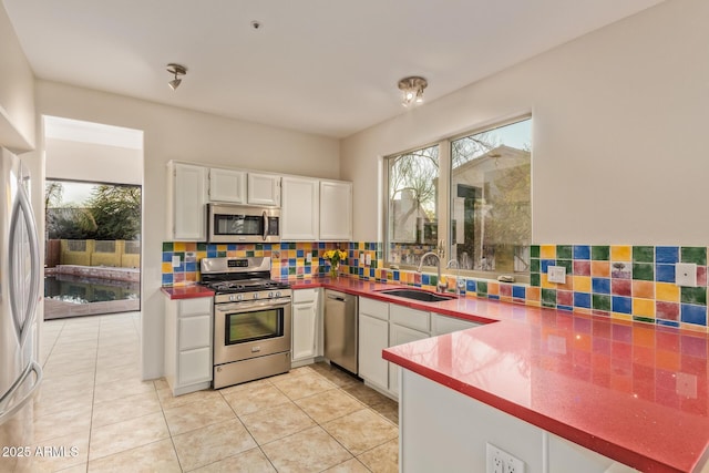 kitchen featuring light tile patterned floors, decorative backsplash, appliances with stainless steel finishes, white cabinetry, and a sink