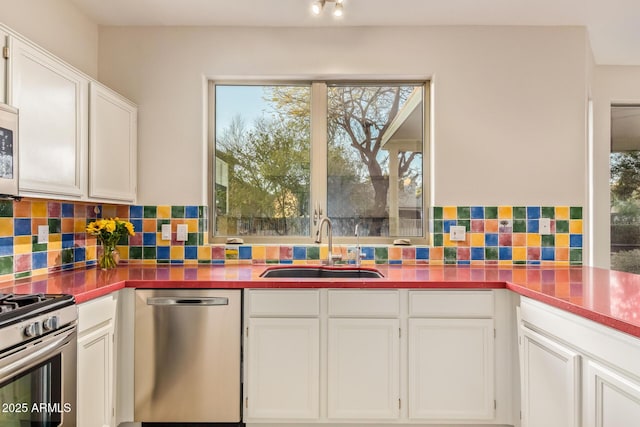 kitchen with appliances with stainless steel finishes, a sink, white cabinetry, and tasteful backsplash