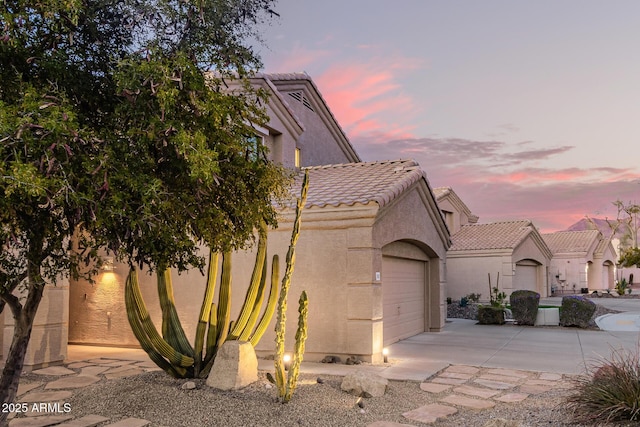 view of front of property with a garage, concrete driveway, a tiled roof, and stucco siding