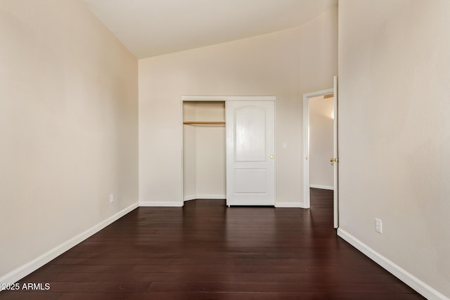 unfurnished bedroom featuring dark wood-type flooring, lofted ceiling, a closet, and baseboards