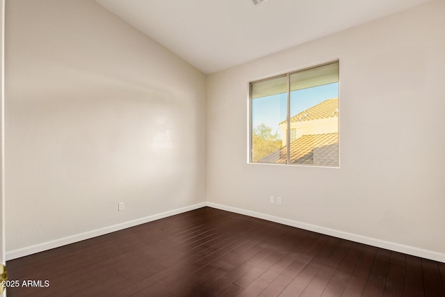 empty room with dark wood-type flooring, vaulted ceiling, and baseboards