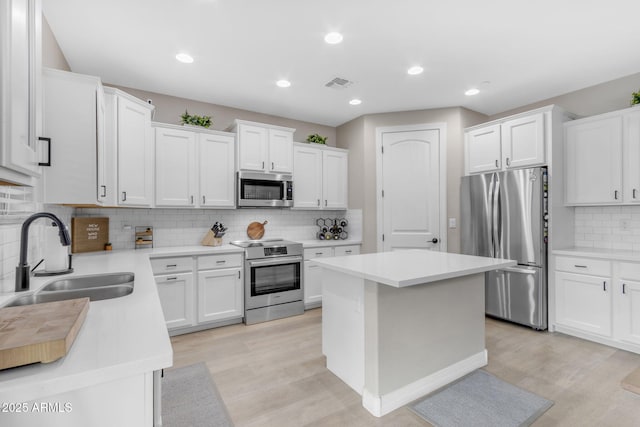 kitchen featuring tasteful backsplash, stainless steel appliances, sink, white cabinets, and a kitchen island