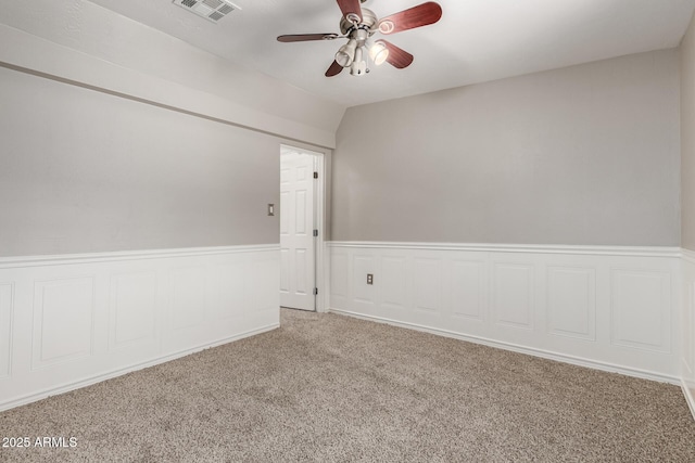 carpeted empty room with a wainscoted wall, a ceiling fan, and visible vents