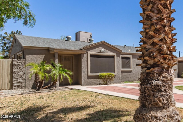 ranch-style home featuring stucco siding, fence, roof with shingles, and a front yard
