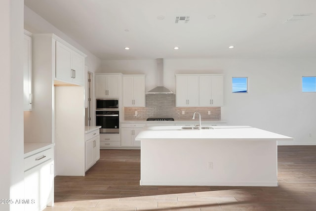 kitchen featuring wall chimney range hood, white cabinetry, a center island with sink, black gas stovetop, and stainless steel oven