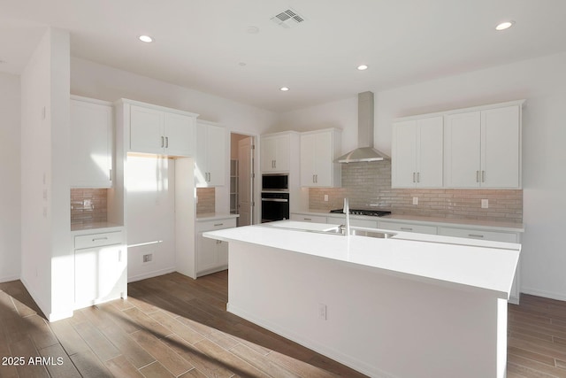 kitchen featuring black appliances, white cabinetry, a center island with sink, and wall chimney exhaust hood