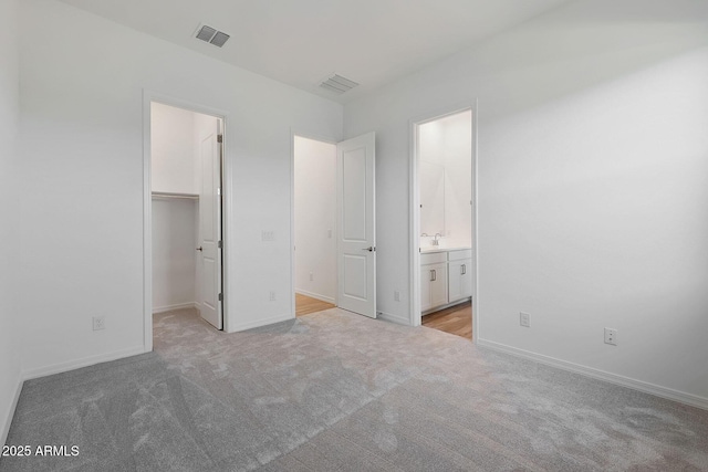 unfurnished bedroom with sink, ensuite bath, a spacious closet, light colored carpet, and a closet