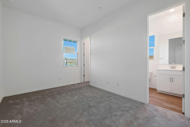 unfurnished bedroom with ensuite bathroom, sink, and dark carpet