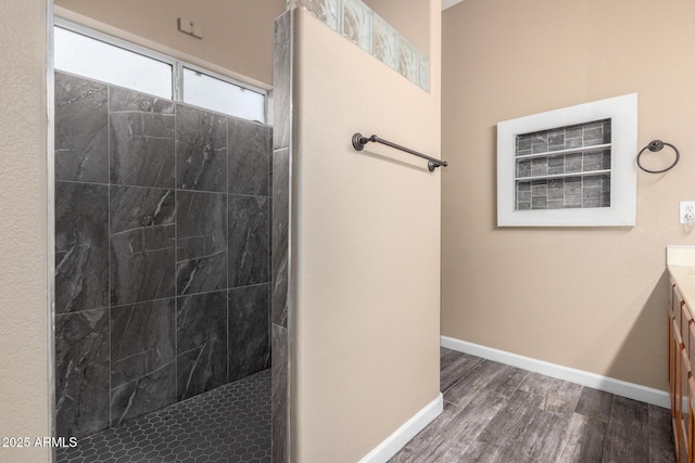 bathroom with a walk in shower, vanity, baseboards, and wood finished floors