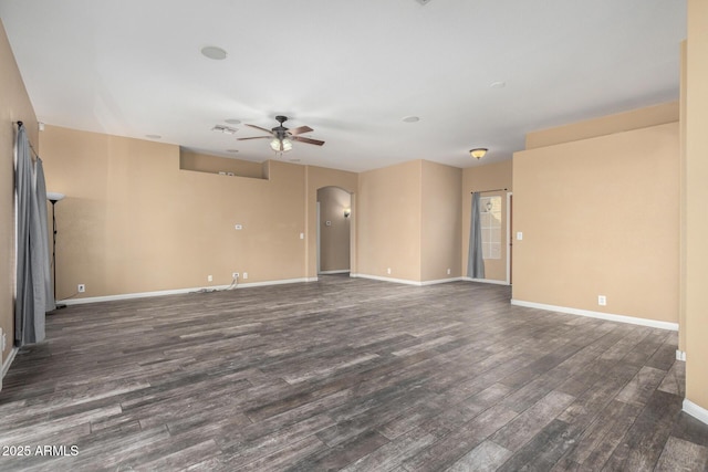 spare room with baseboards, ceiling fan, arched walkways, and dark wood-type flooring