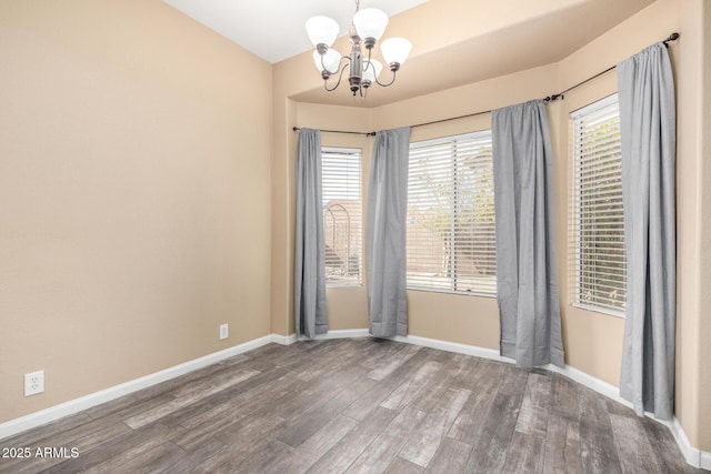 empty room featuring a chandelier, dark wood finished floors, and baseboards