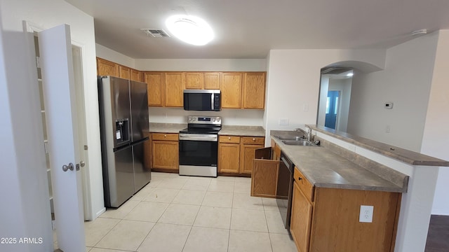 kitchen with light tile patterned floors, brown cabinetry, a peninsula, black appliances, and a sink