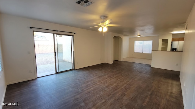 spare room with dark wood-style floors, plenty of natural light, arched walkways, and visible vents