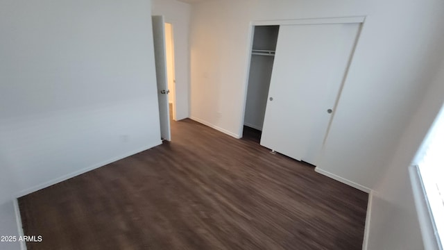 unfurnished bedroom featuring a closet, dark wood finished floors, and baseboards