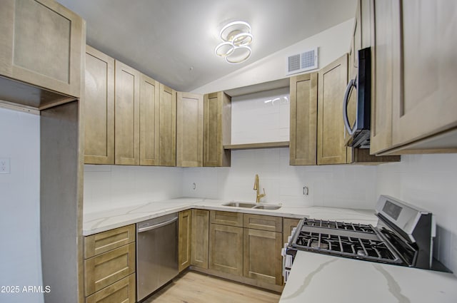 kitchen featuring appliances with stainless steel finishes, light wood-type flooring, light stone counters, sink, and lofted ceiling