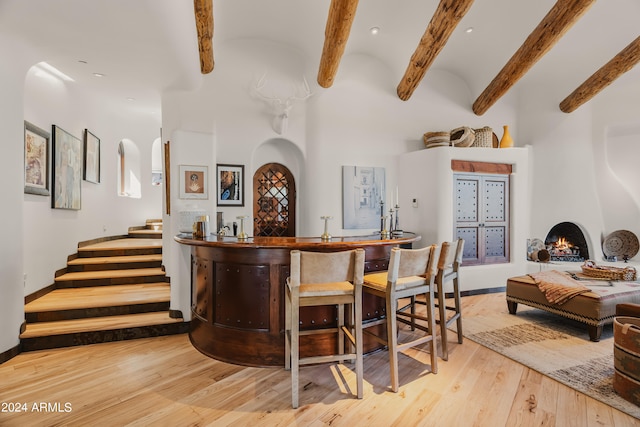 bar with light hardwood / wood-style floors, beamed ceiling, and a large fireplace