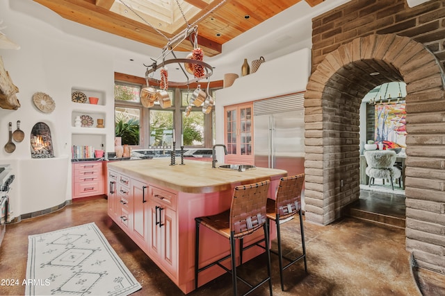 kitchen featuring a kitchen bar, butcher block countertops, built in fridge, wooden ceiling, and a kitchen island with sink