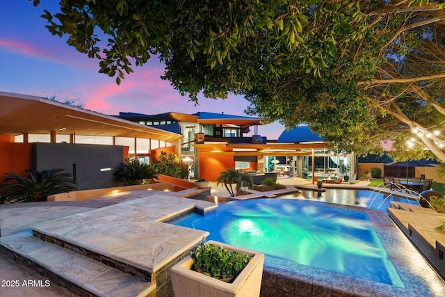 pool at dusk featuring pool water feature, an in ground hot tub, and a patio