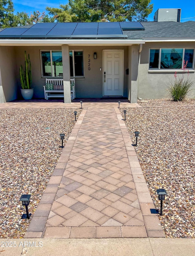 property entrance featuring covered porch, roof mounted solar panels, and stucco siding