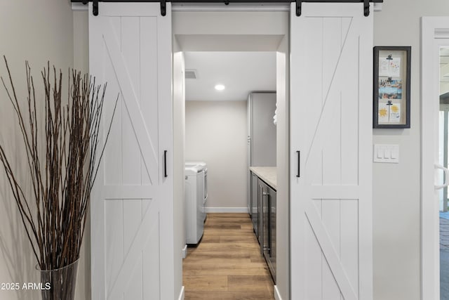laundry room featuring a barn door, baseboards, light wood finished floors, washer and clothes dryer, and laundry area