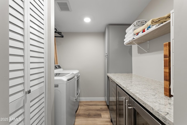 laundry area featuring cabinet space, light wood-type flooring, visible vents, washing machine and clothes dryer, and baseboards