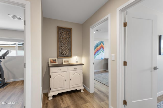 hall with baseboards, visible vents, and wood finished floors
