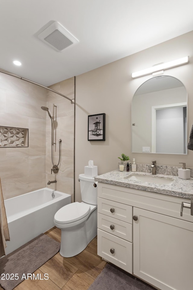 bathroom featuring toilet, wood finished floors, vanity, visible vents, and washtub / shower combination