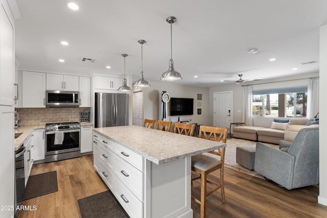 kitchen with recessed lighting, visible vents, a kitchen breakfast bar, open floor plan, and appliances with stainless steel finishes