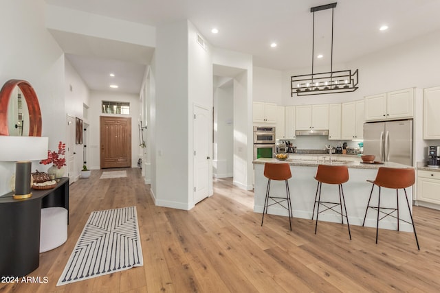 kitchen featuring stainless steel appliances, hanging light fixtures, light hardwood / wood-style floors, and white cabinetry