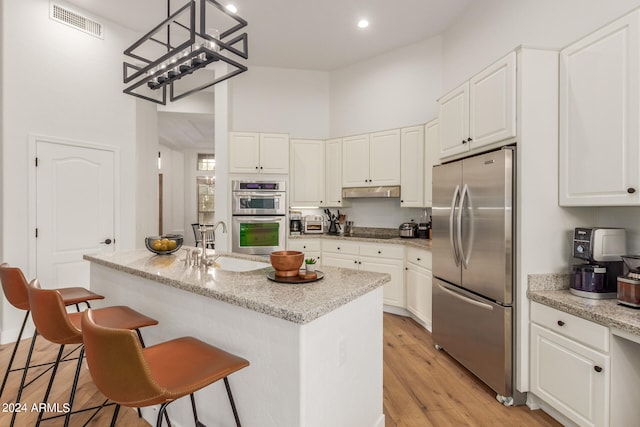 kitchen with light hardwood / wood-style flooring, a center island with sink, sink, light stone countertops, and appliances with stainless steel finishes