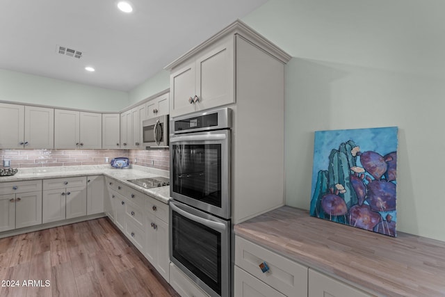 kitchen with white cabinets, tasteful backsplash, light stone countertops, light hardwood / wood-style flooring, and stainless steel appliances