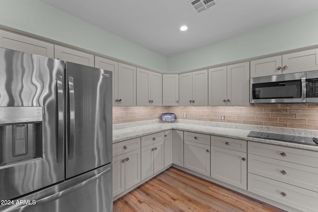 kitchen featuring light stone counters, stainless steel appliances, decorative backsplash, and light wood-type flooring