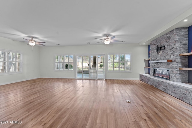 unfurnished living room with light hardwood / wood-style floors, ceiling fan, a fireplace, and a wealth of natural light