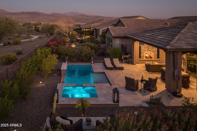 view of swimming pool with a pool with connected hot tub, an outdoor living space with a fireplace, a patio area, fence, and a mountain view